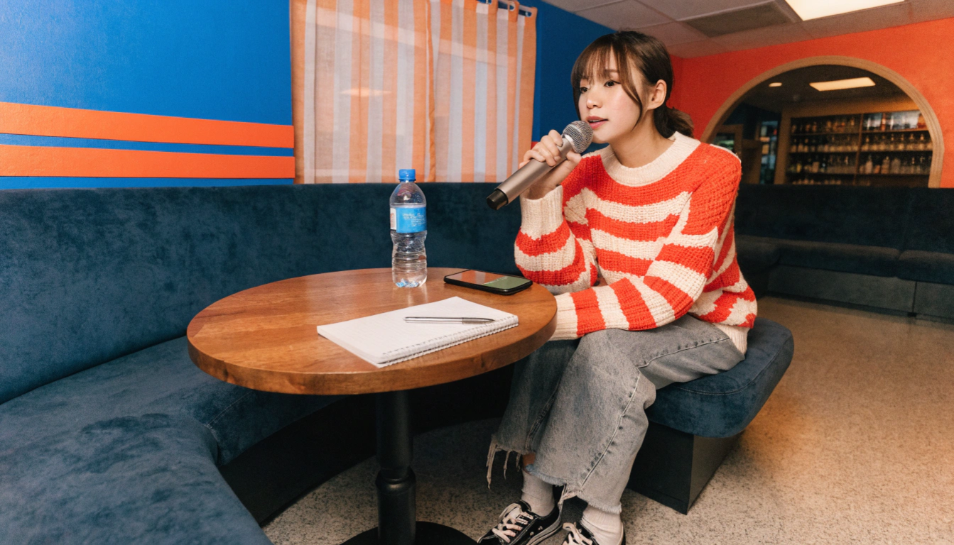 明るい色調のカラオケボックスを舞台に、20代の日本人女性が正しい姿勢と呼吸を意識して歌う様子を描く。